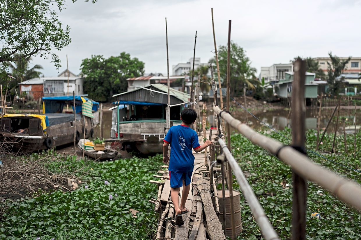 Trung walking along a weathered bridge built with bamboo poles and wooden planks to reach a houseboat he shares Tran and Thuy.— AP