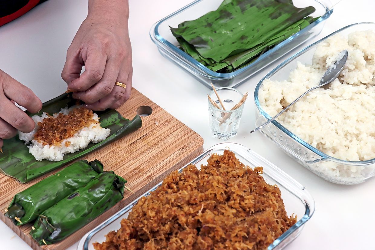 Press one heaping tablespoon of pulut in the middle of the banana leaf and spread two teaspoons of filling along the length of the pulut, then roll into a log and seal the ends with toothpicks.