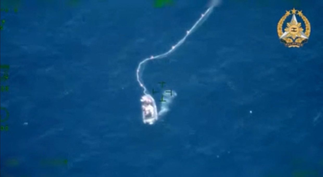 In this handout frame grab from an aerial video footage taken on March 23, 2024 and released by the Armed Forces of the Philippines (AFP), a vessel identified by the Armed Forces of the Philippines (AFP) as Chinese rigid-hull inflatable boat (RHIB) installs a floating barrier during a Philippine supply mission near Second Thomas Shoal in the disputed South China Sea. - AFP