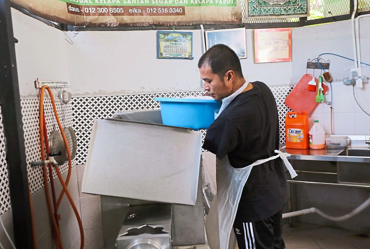 Hard at work: Mohd Firdaus using a machine to squeeze coconut milk when met at Kampung Sungai Rokam in Ipoh. 