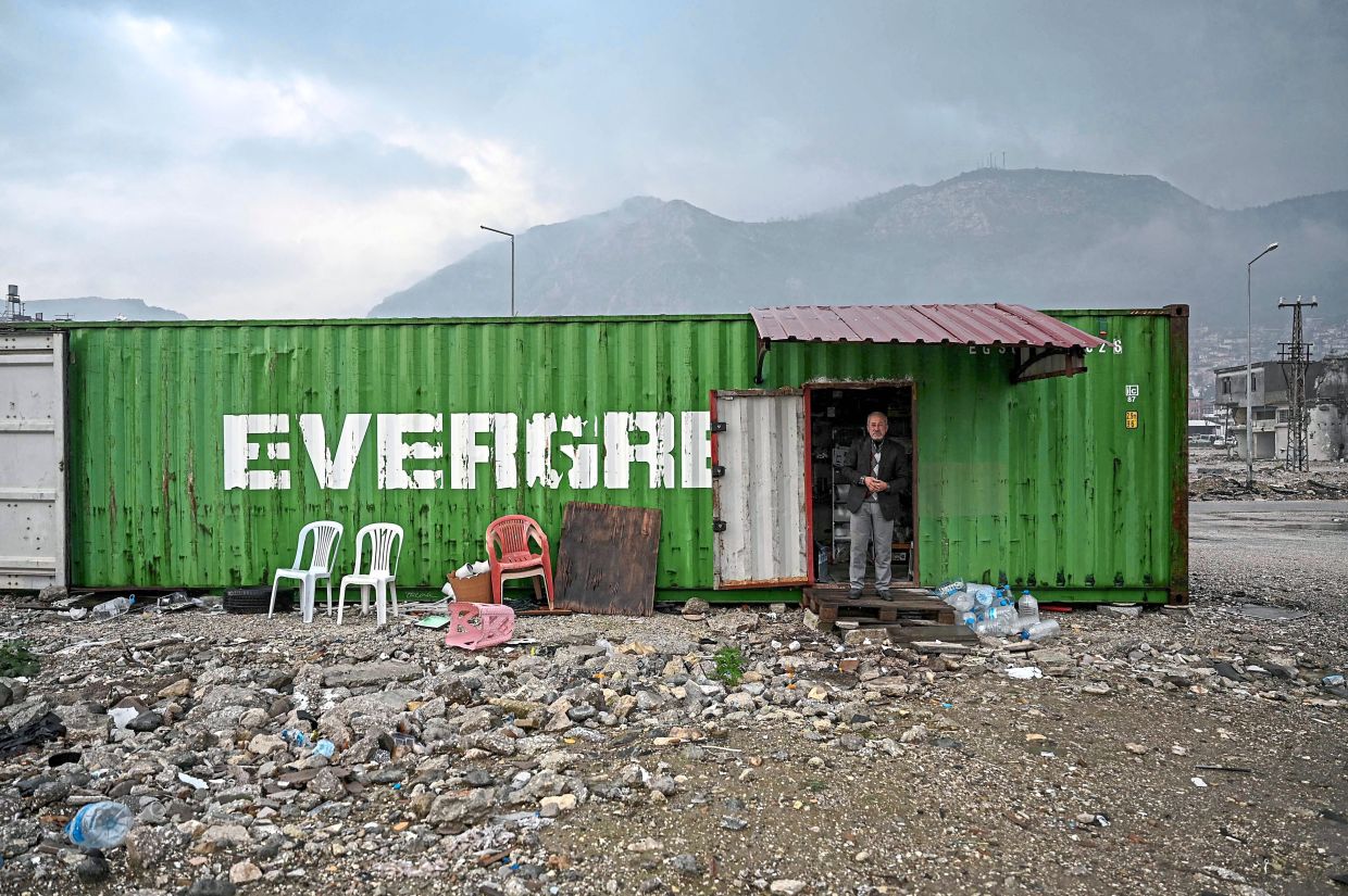 Sislioglu standing at the door of his container shop erected on empty land after the rubble of destroyed buildings was cleared following the February 2023 earthquake in the centre of Antakya; 