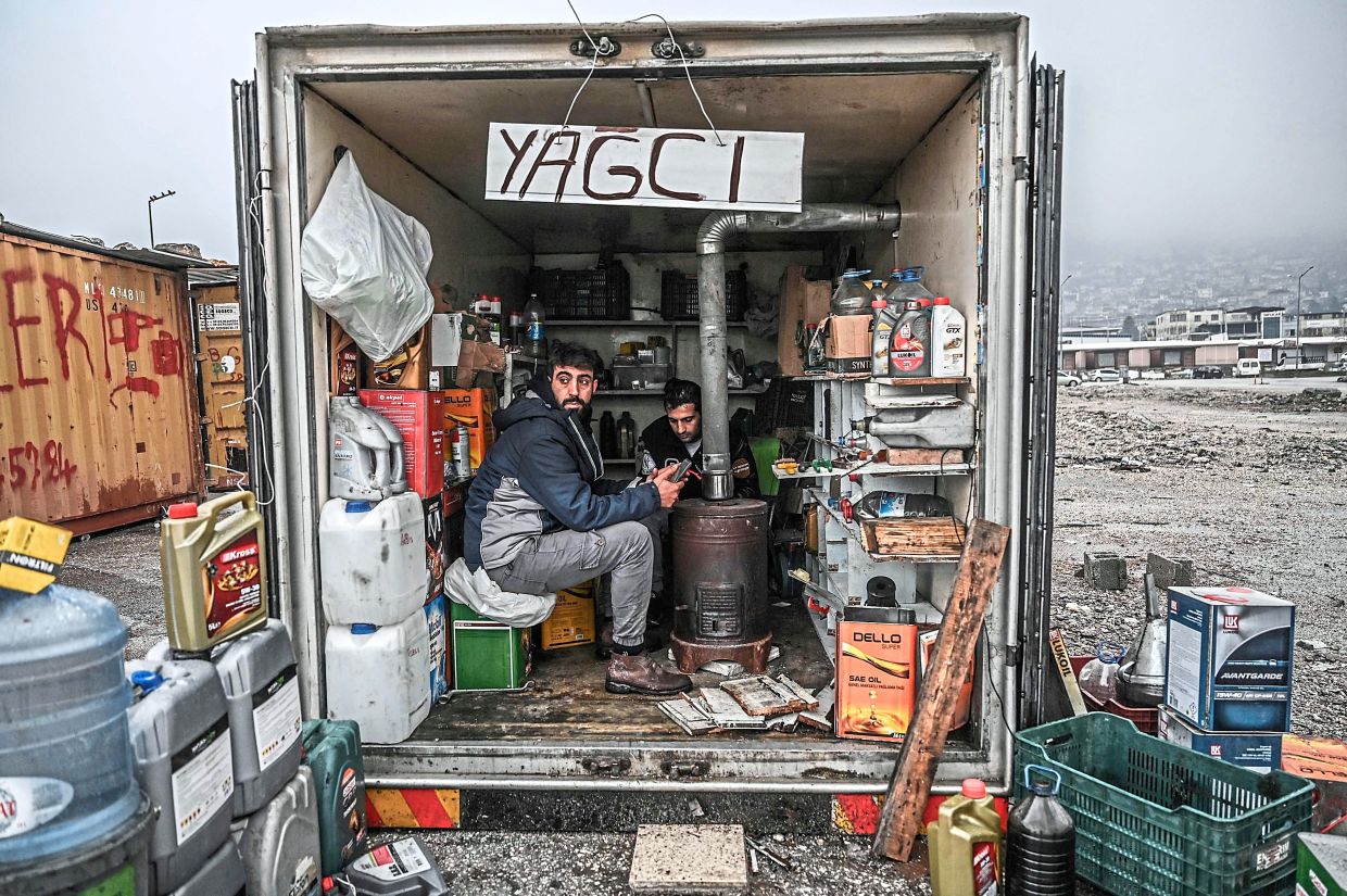 Two men warm their hands at a stove inside a container converted into a workshop in Turkiye’s mountainous southeast. — AFP