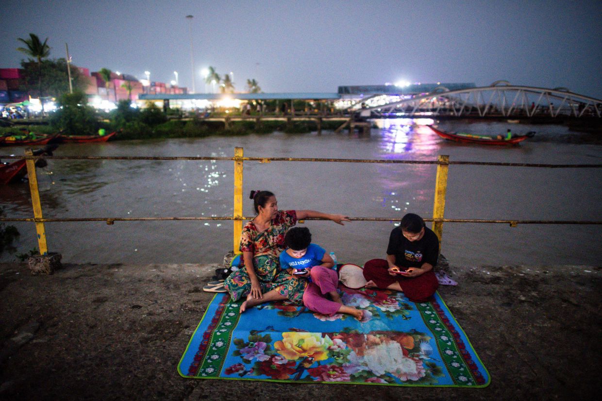 People gather at a jetty during an electricity blackout in Yangon on April 26, 2024. As the sun sets on another scorching Yangon day, the hot and bothered descend on the Myanmar city's parks, the coolest place to spend an evening during yet another power blackout. For many in the city of some eight million, relief comes only at night and outdoors with the metropolis' parks offering natural shade and blissful breezes. - AFP