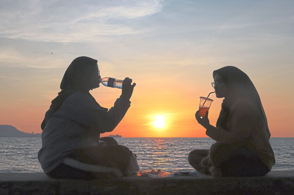 A couple of friends quenching their thirst while enjoying the sunset at Pantai Robina.