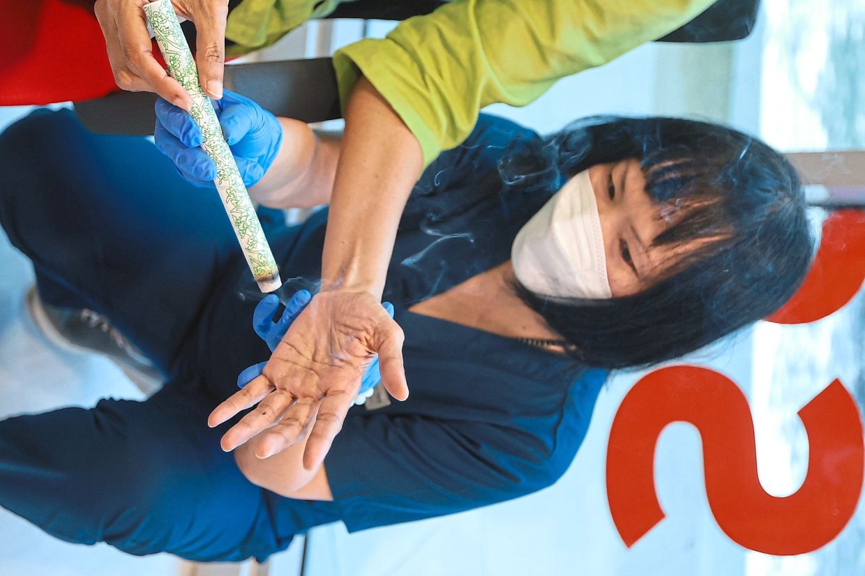 Dr Ong guides a patient on how to use the moxa stick, via the indirect method, at the clinic, so that she can safely do it herself at home.
