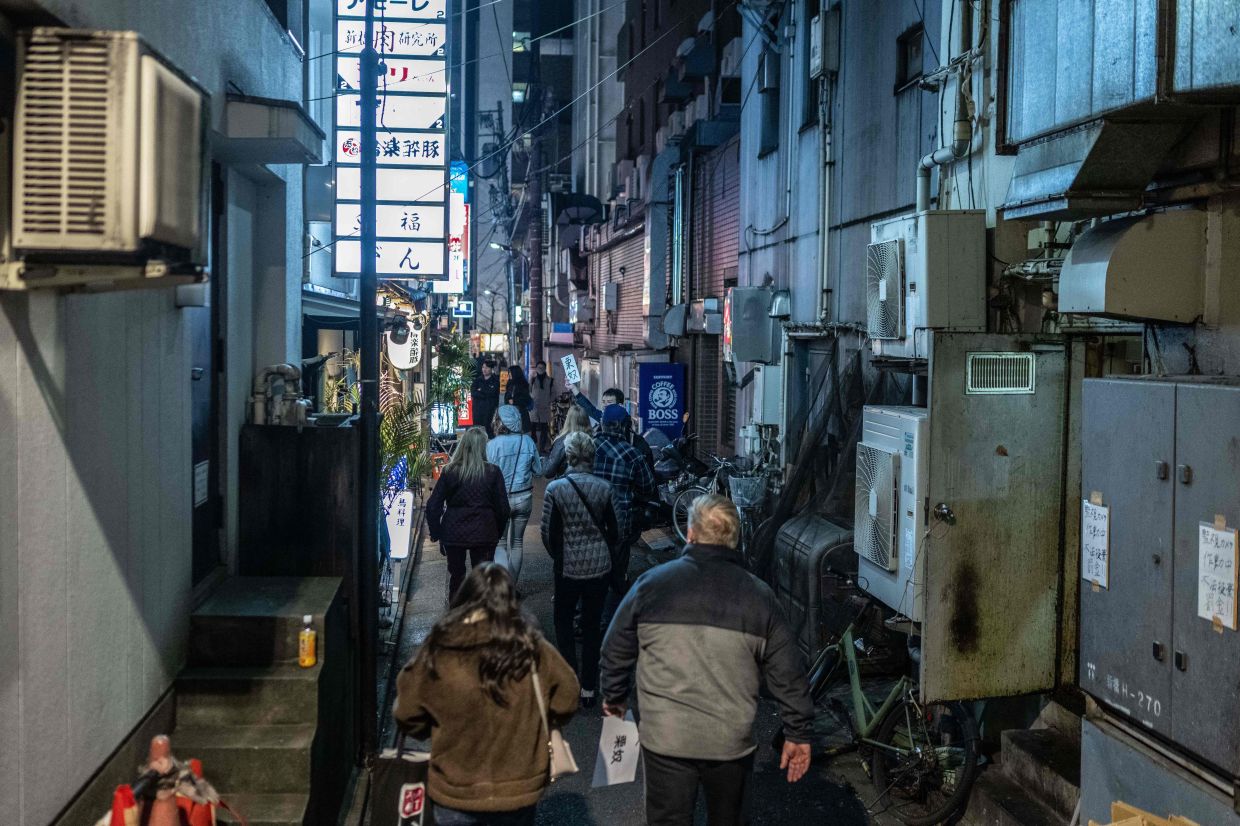 Tourists from the US walking down a small alleyway as they take part in a snack bar tour in Tokyo.