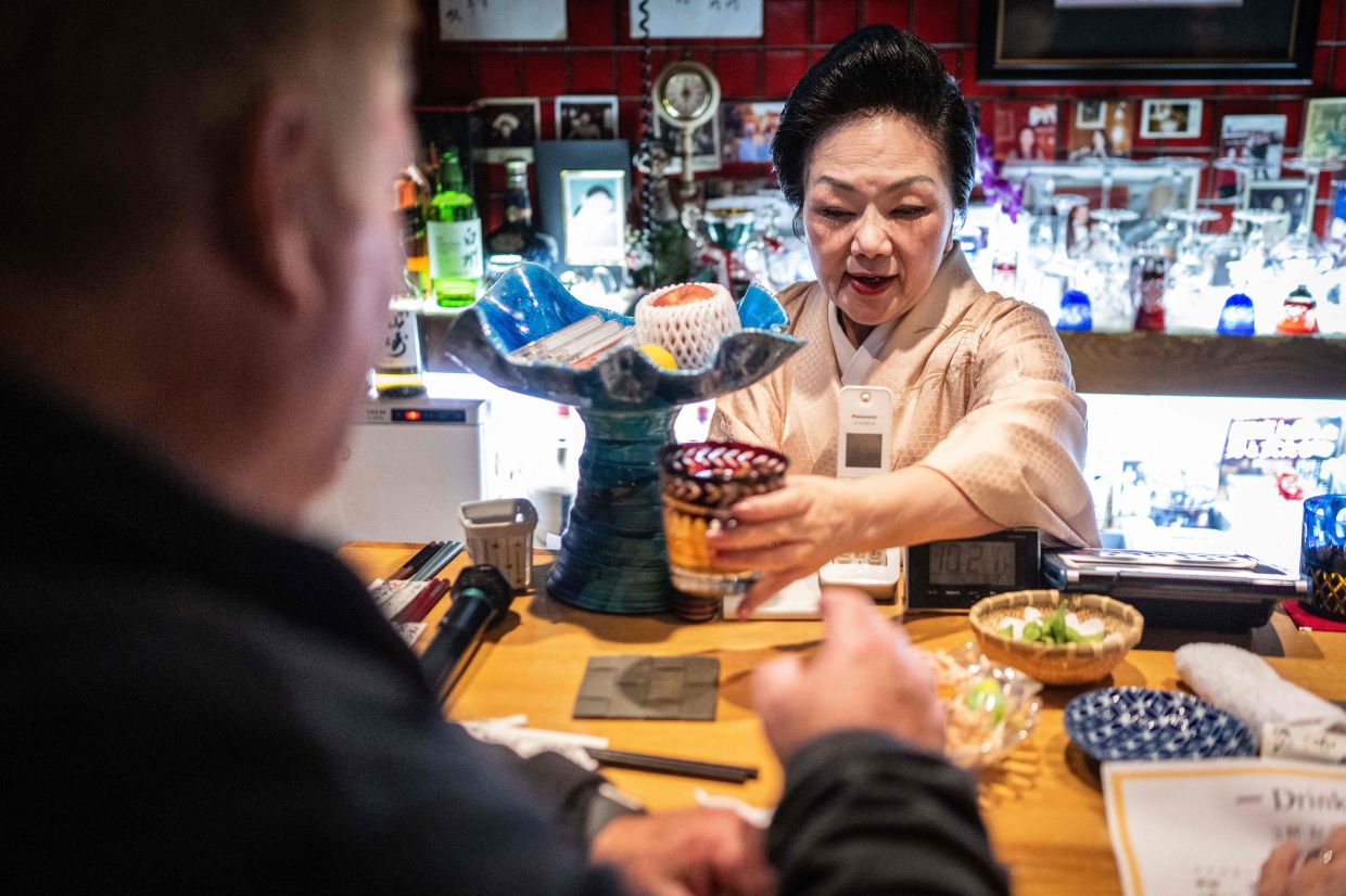Kuri Awaji serving a drink to a tourist from the US taking part in a snack bar tour at her bar 'Kuriyakko' in Tokyo.