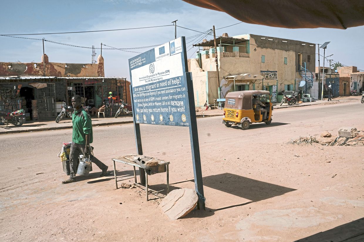 A man passing by a sign from the UN International Organisation of Migration in Agadez, Niger, listing tips for migrants seeking help. — ©2024 The New York Times Company