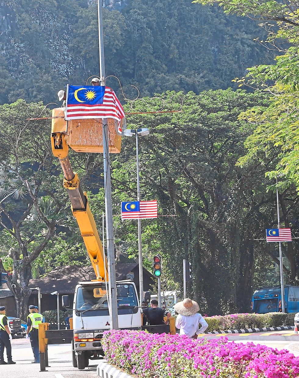 Symbolic gesture: Workers putting up the Jalur Gemilang onto street light poles along Jalan Tambun in Ipoh. — Bernama