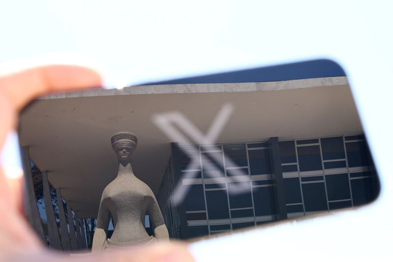 FILE PHOTO The logo of social media platform X is seen on a mobile phone next to a reflection of Brazils Supreme Court in this illustration taken August 30 2024 in Brasilia Brazil.   REUTERSUeslei MarcelinoFile Photo