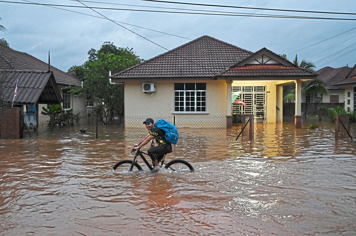 Keeping spirits high: A young man cycling through floodwaters to deliver necessities to a shelter in Kuala Nerus, Terengganu. — Bernama