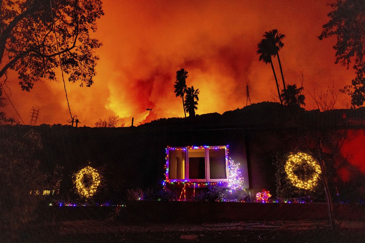 A helicopter drops water on the Palisades fire behind a home with Christmas lights in Mandeville Canyon in Los Angeles on Jan 10. Photo: AP 