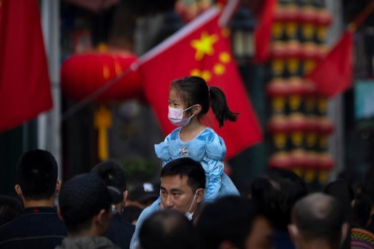 A  girl wearing a face mask rides on a man's shoulders as they walk along a tourist shopping street in Beijing, Oct. 7, 2022. China has announced its first overall population decline in recent years amid an aging society and plunging birthrate. -- Photo: AP
