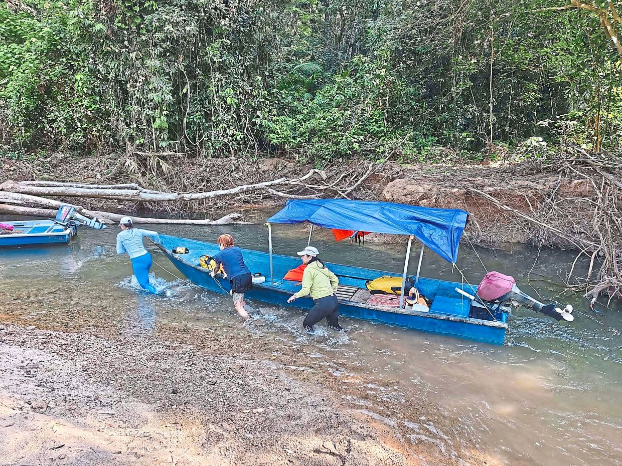 Campers pushing a fibreglass boat up a river on the way to the campsite.