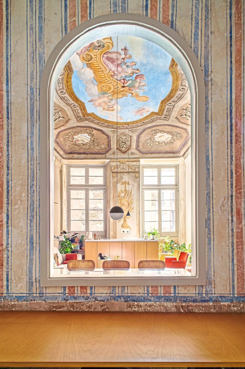 The main room of the renovated palace can be seen under its frescoed ceiling through an arched opening.