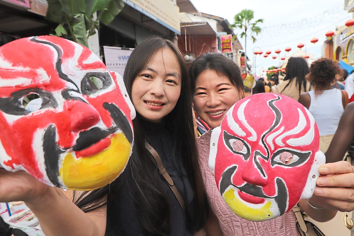 Xing (left) with Rao Ying Zi from China, holding Chinese opera masks that they painted at the Penang Miaohui event.