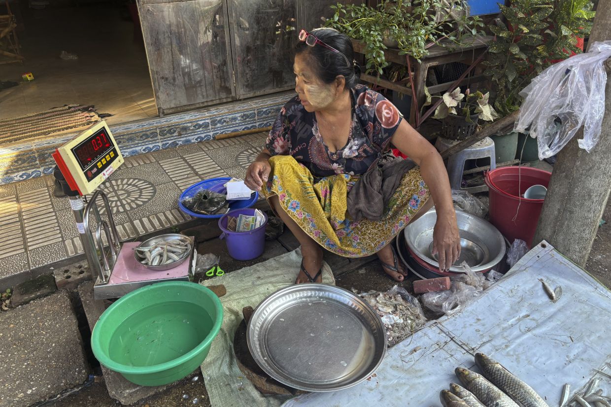 A woman in Yangon, Myanmar, applies thanakha, a traditional makeup, while weighing fish for customers at a local bazaar. Photo: AP
