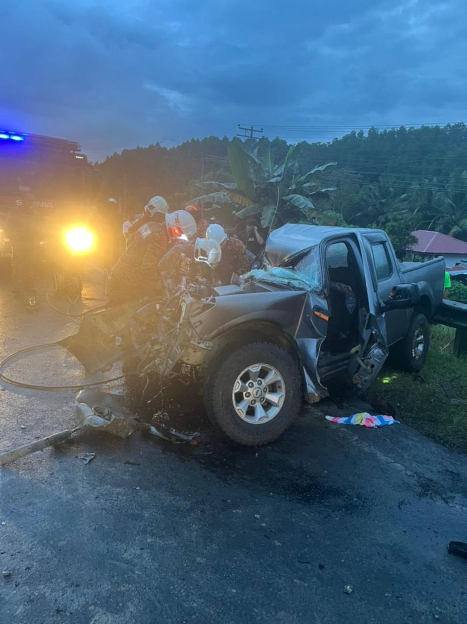 Firemen extricating the body from the wrecked four-wheel-drive vehicle that collided with a lorry in Tuaran on Friday (Feb 21).