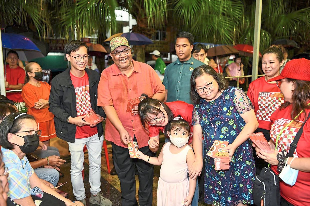 Amirul Azizan (wearing cap) and Siew Ki (on his left, in red) giving ang pow to kids. (Right photo) Mohamad Zahri using a brush to put finishing touches to a Chinese calligraphy painting celebrating the Year of the Wood Snake.