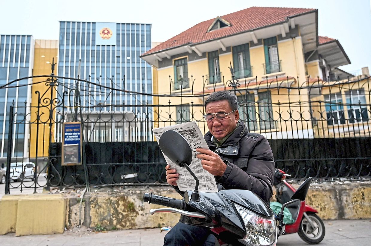 Uncertain times: A man reading a newspaper in front of the Ministry of Transport in Hanoi. — AFP