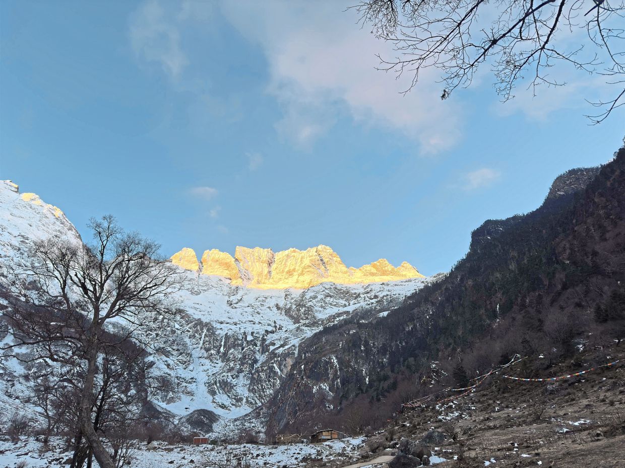 The frozen Sacred Waterfall, with the Meili Snow Mountains covered in golden sun rays in the background.