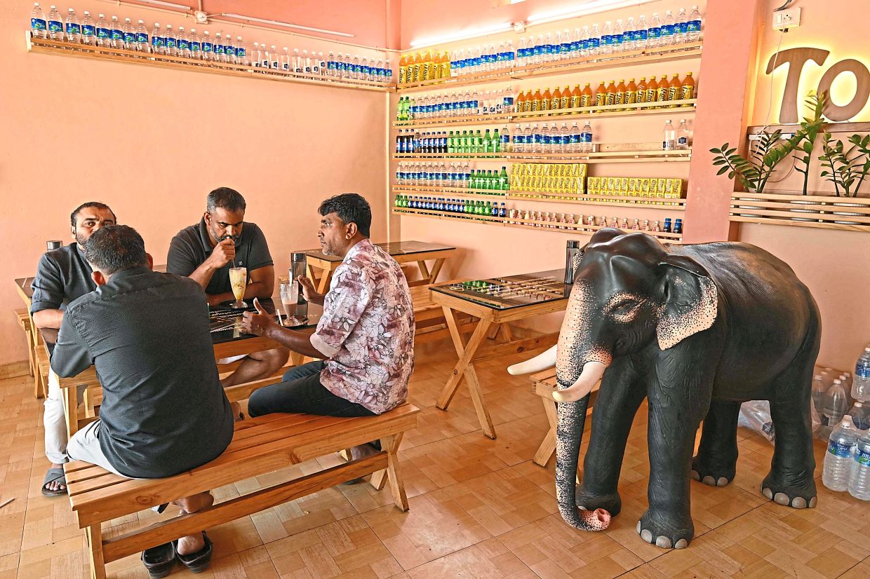 Customers sitting next to an elephant model placed inside a coffee shop.