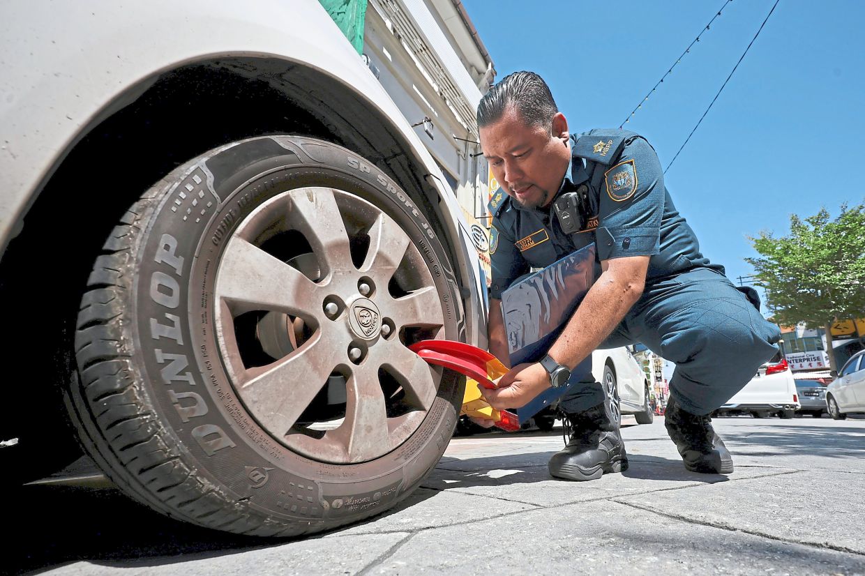 An MBPP enforcement officer clamping the wheel of an illegally parked car on Campbell Street.