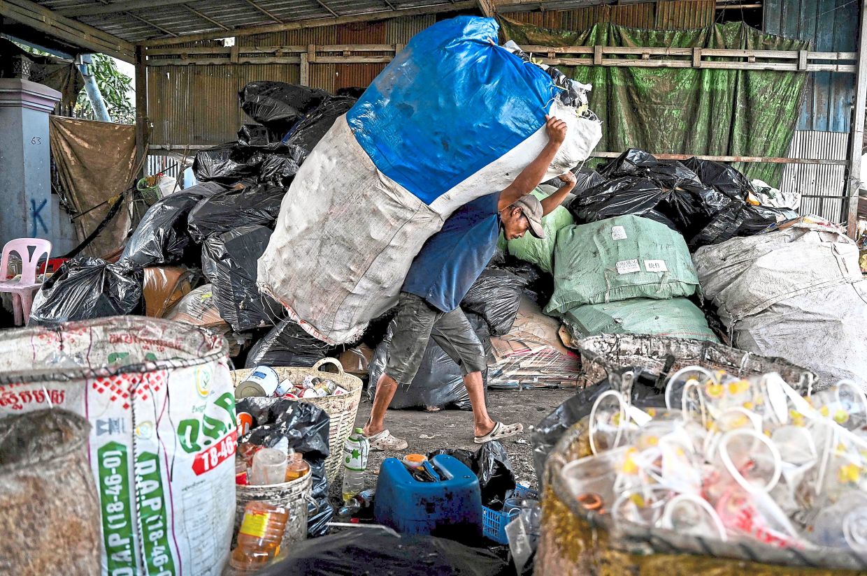 A worker carrying a bag containing plastic bottles at a recycling depot on the outskirts of Phnom Penh. — AFP