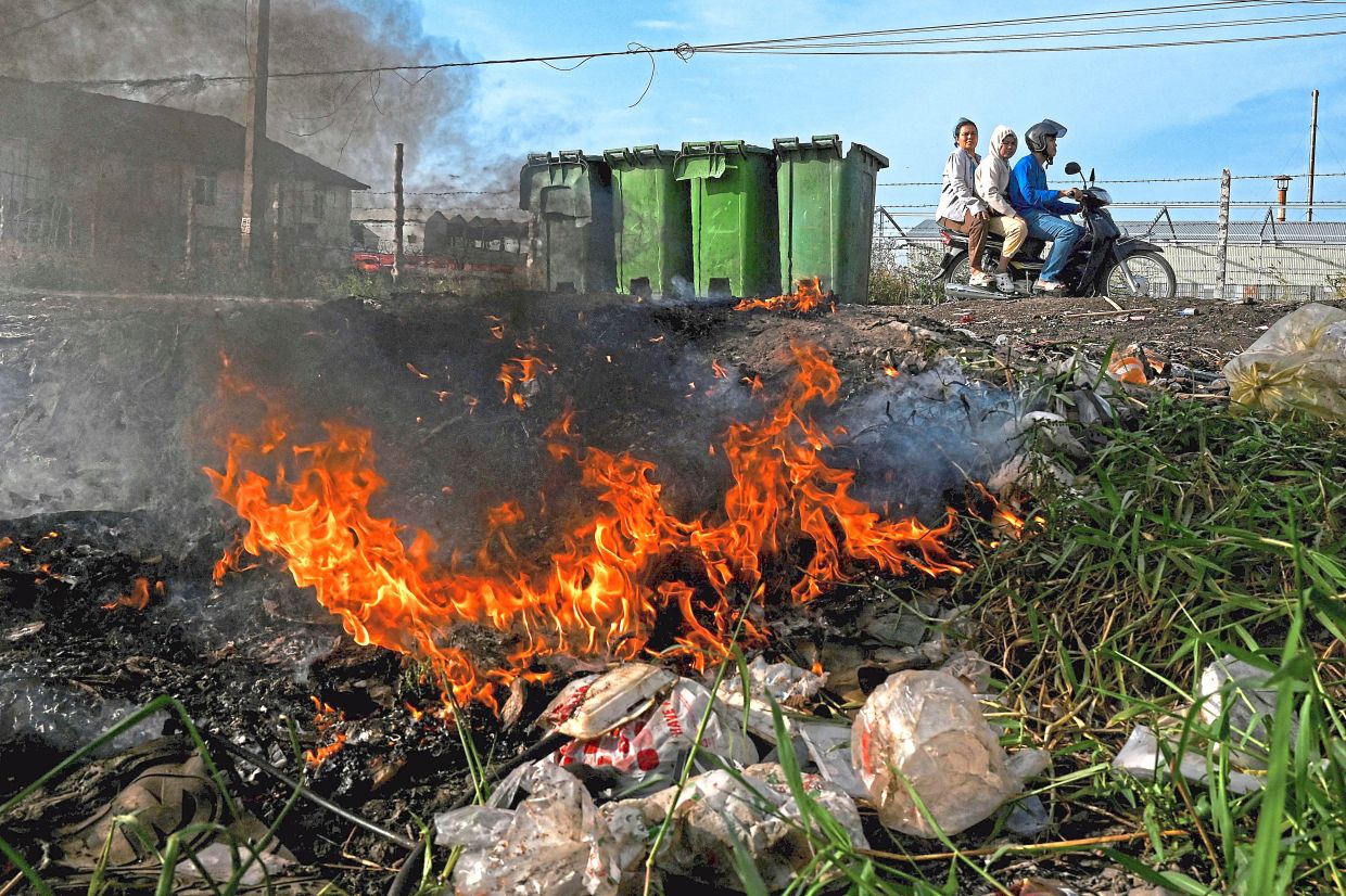 People travelling on a motorbike past burning plastic waste on the outskirts of Phnom Penh. — AFP