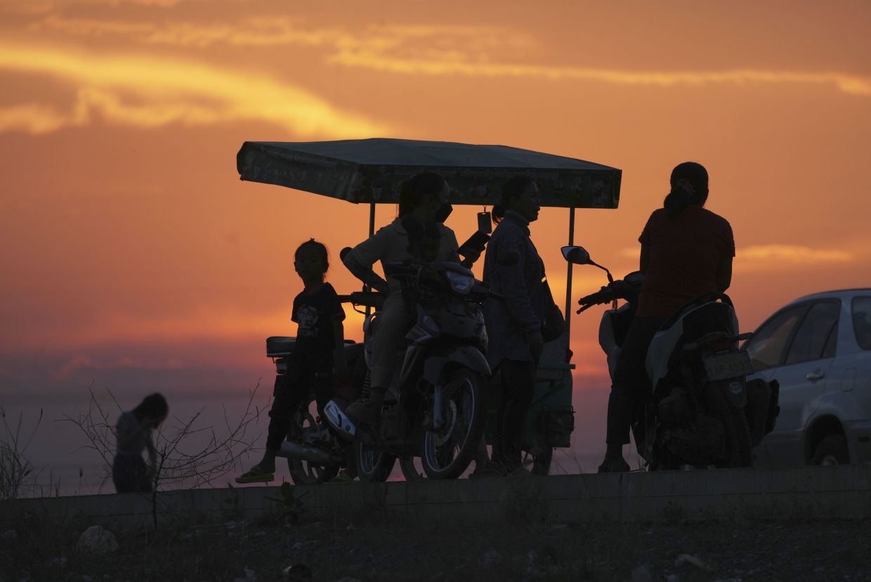 Local visitors are silhouetted against the setting sun as they buy snacks at Chong Tnol, outside Phnom Penh Cambodia. -- AP Photo/Heng Sinith