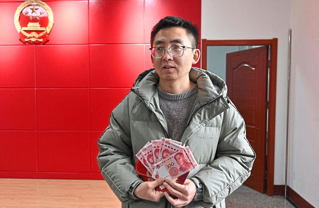 Good payoff: Wang showing the cash he received from the local government after his marriage in early January, at an administrative office in Luliang. — AFP