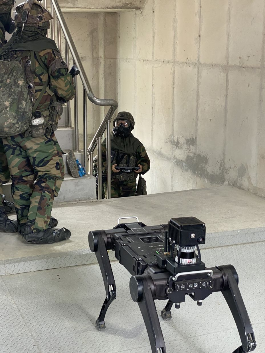 A multipedal robot stands behind army personnel as its operator climbs the stairs. - Photo: The Korea Herald