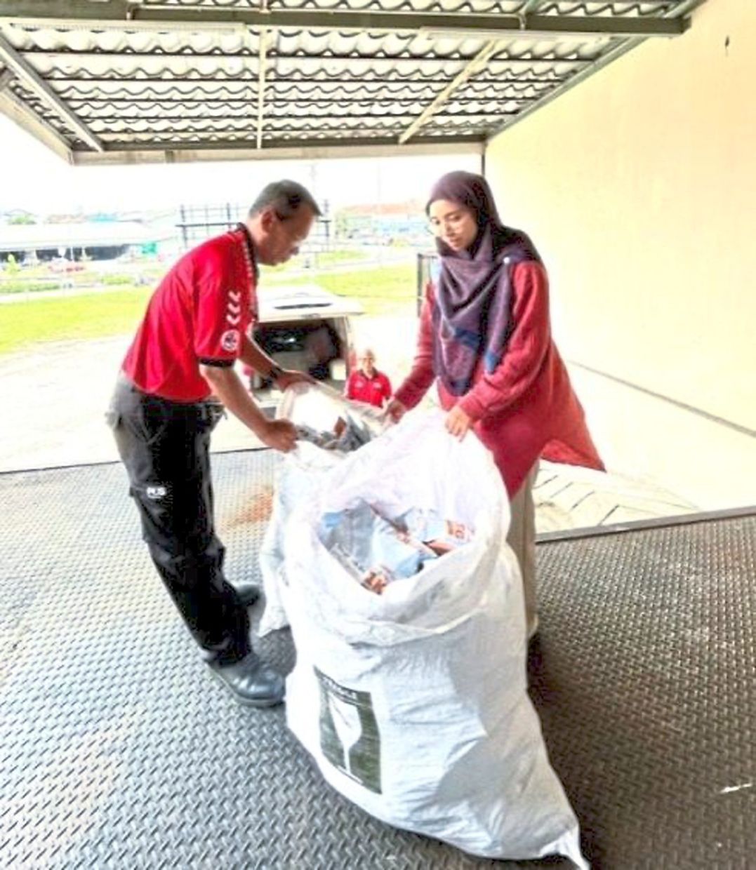 A pharmacy unit staff member handing over bundles of medicine to PosLaju workers, ready for delivery to patients. 