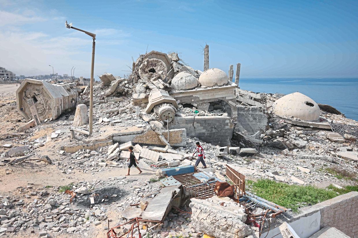 Palestinians walking beside the destroyed Abdul Aziz al-Khalidi mosque in Gaza.The Israelis have bombed Palestine to the ground, killing thousands. The Zionist state now wants to move these people away from their homeland. — AFP