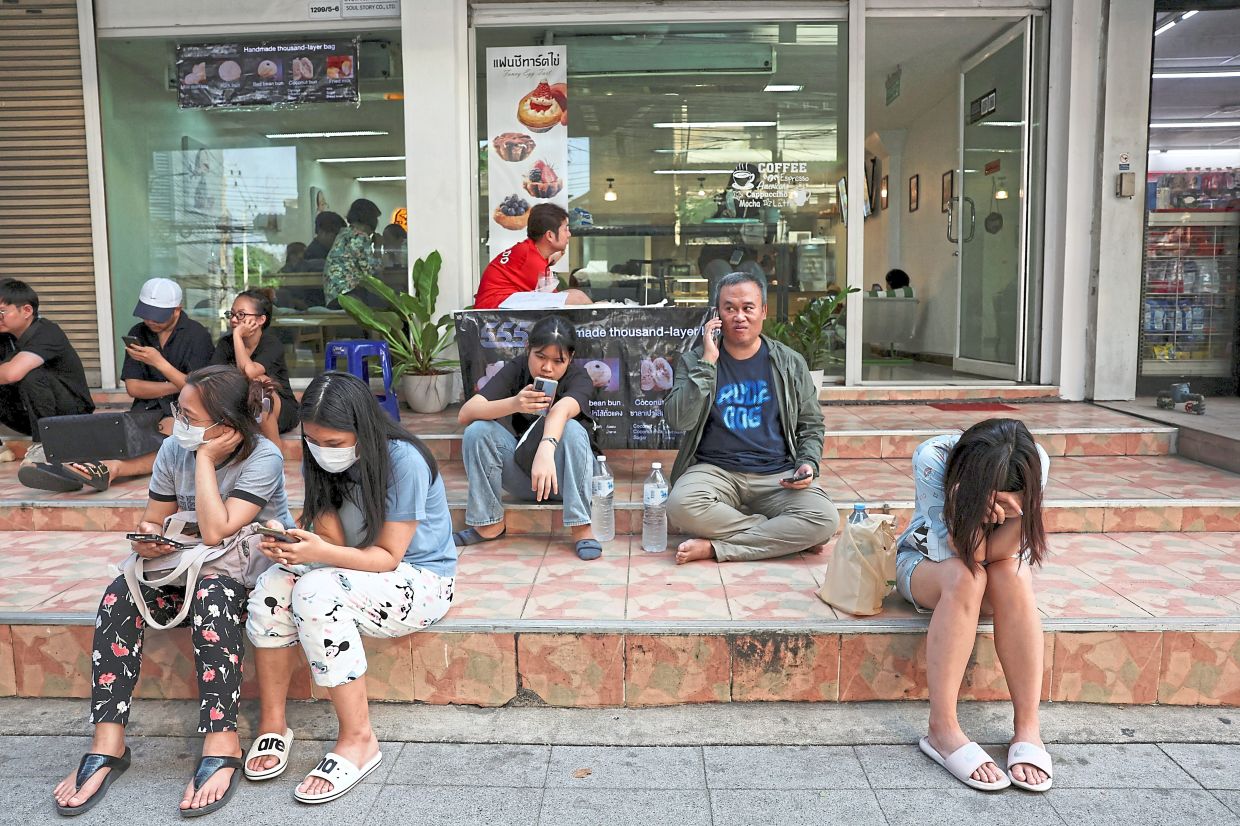 Unwelcome shock: People sitting in front of a shop in Bangkok after the strong earthquake struck central Myanmar. — Reuters