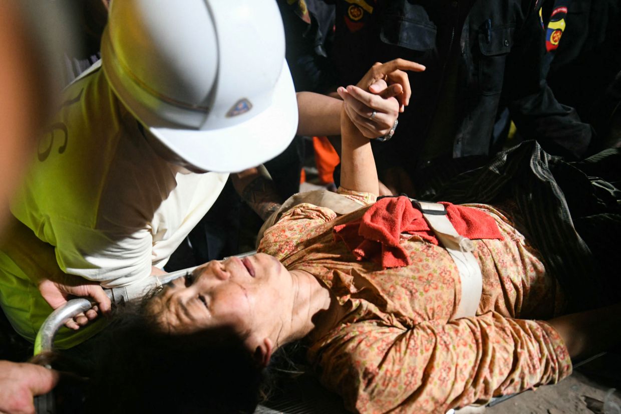 Ye Aung accompanies his wife Phyu Lay Khaing on their way to the hospital after she was rescued from the rubble of the collapsed Sky Villa Condo apartment building in Mandalay on March 29, 2025, a day after an earthquake struck central Myanmar. The death toll from a huge earthquake that hit Myanmar and Thailand passed 1,000 on March 29, as rescuers dug through the rubble of collapsed buildings in a desperate search for survivors. -- Photo by Sai Aung MAIN / AFP