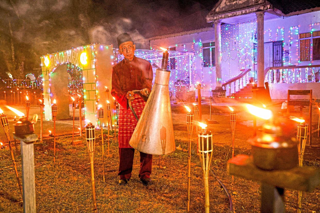 Villager Mahli Udin lighting a giant lamp along with other oil lamps to decorate his house at Kampung No.5 in Kuching, Sarawak. — Photos: RONNIE CHIN, FAIHAN GHANI, ZHAFARAN NASIB and ZULAZHAR SHEBLEE/The Star