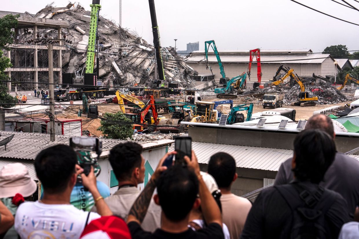 People taking a picture as machinery is used to clear the rubble at the site of an under-construction building collapse in Bangkok on March 31, 2025. - AFP