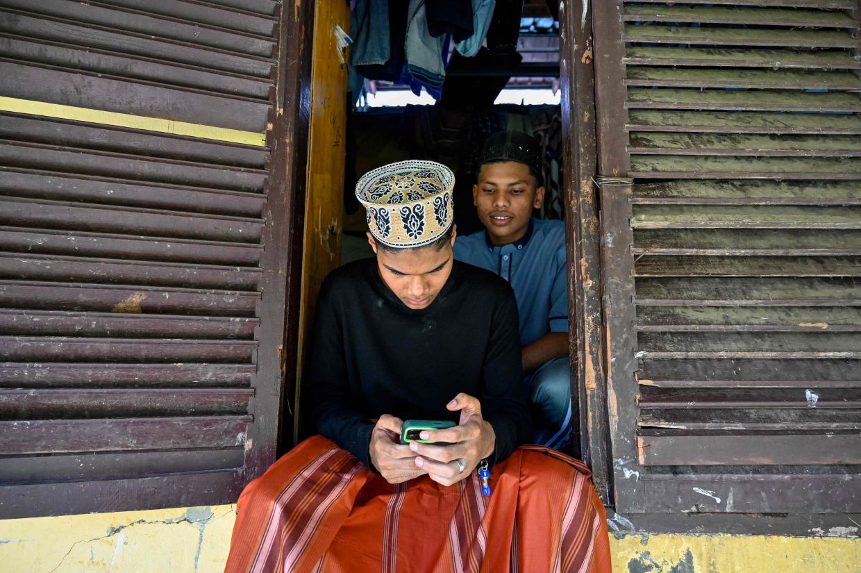A Rohingya refugee checkingcalling his family after taking part in Aidil Fitri prayers at a shelter in Padang Tiji in Aceh on March 31, 2025. - AFP