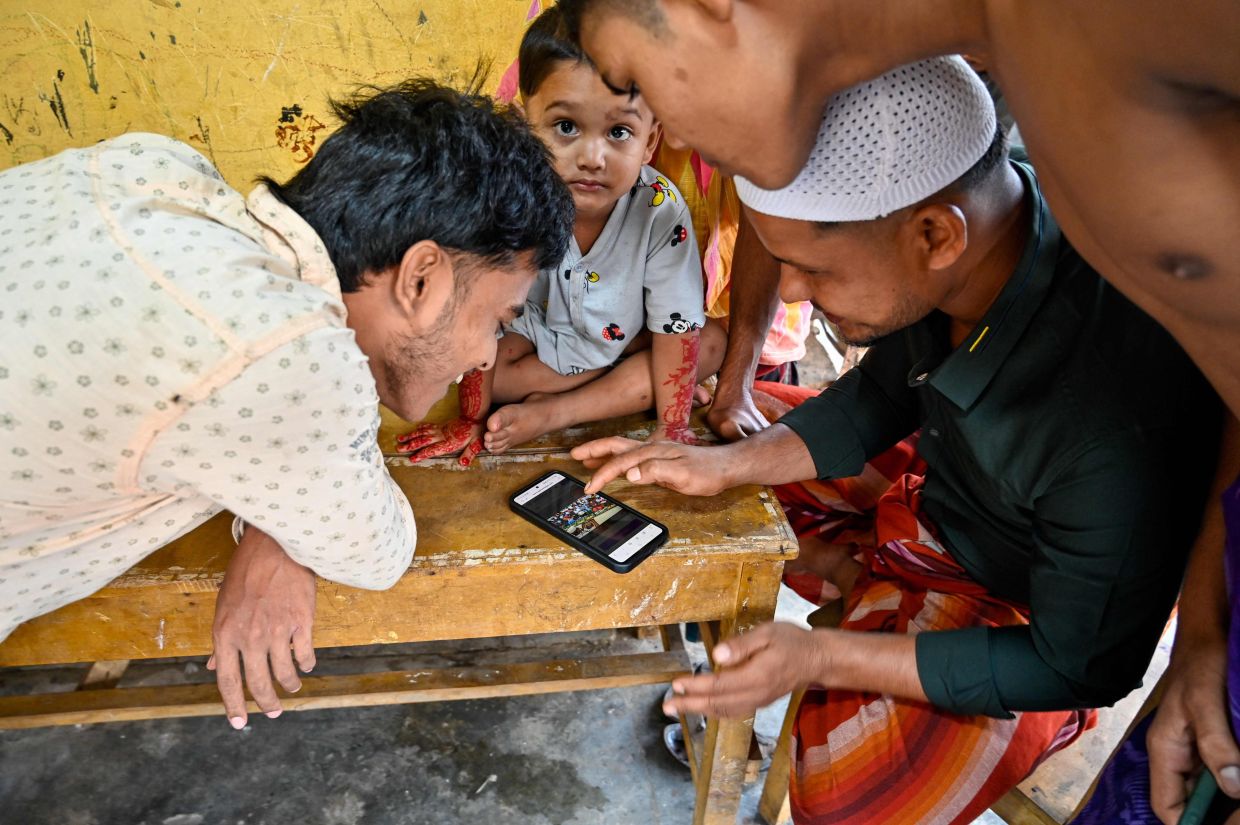 Rohingya refugees gathering around a smartphone as they get in touch with family members in Myanmar before taking part in Aidil Fitri prayers at the shelter in Padang Tiji, Aceh on March 31. - AFP
