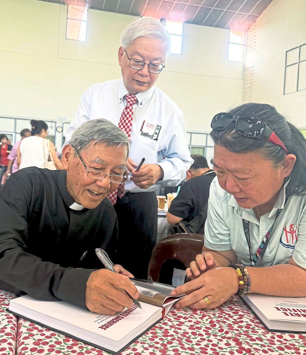Father Cosmas signing his book for a customer while Opus Publication director Datuk CL Chan looks on.