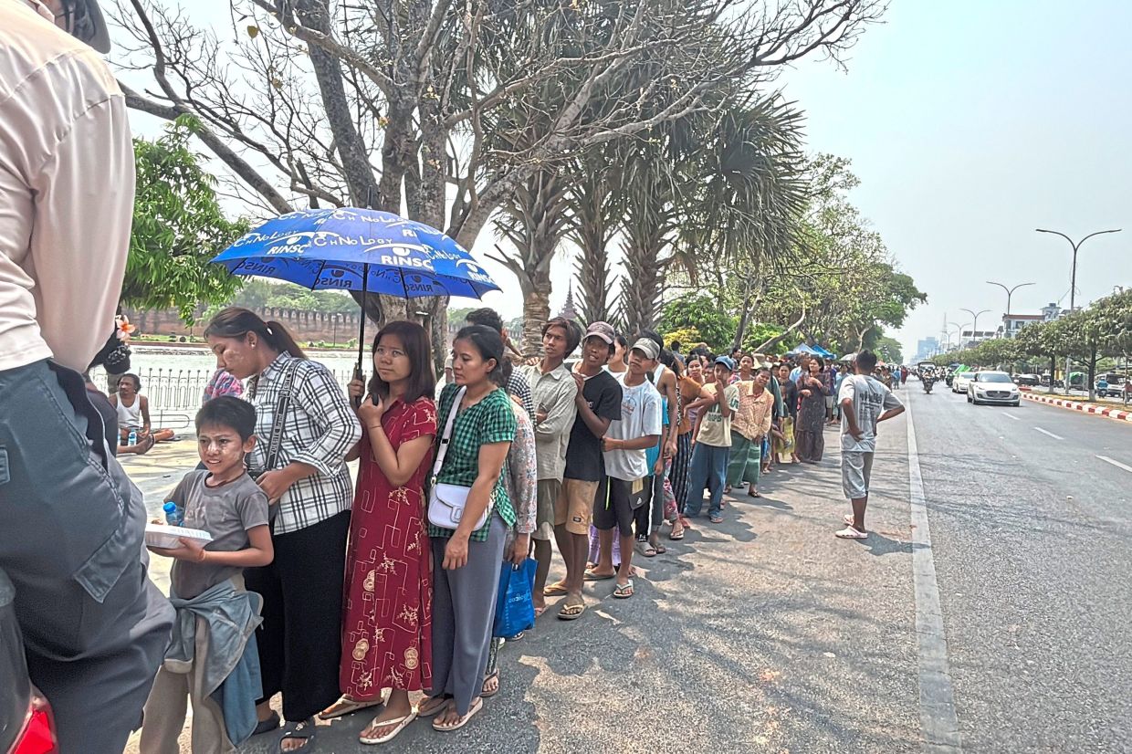 Making do: Quake survivors lining up on a roadside for free food in Mandalay. — AP