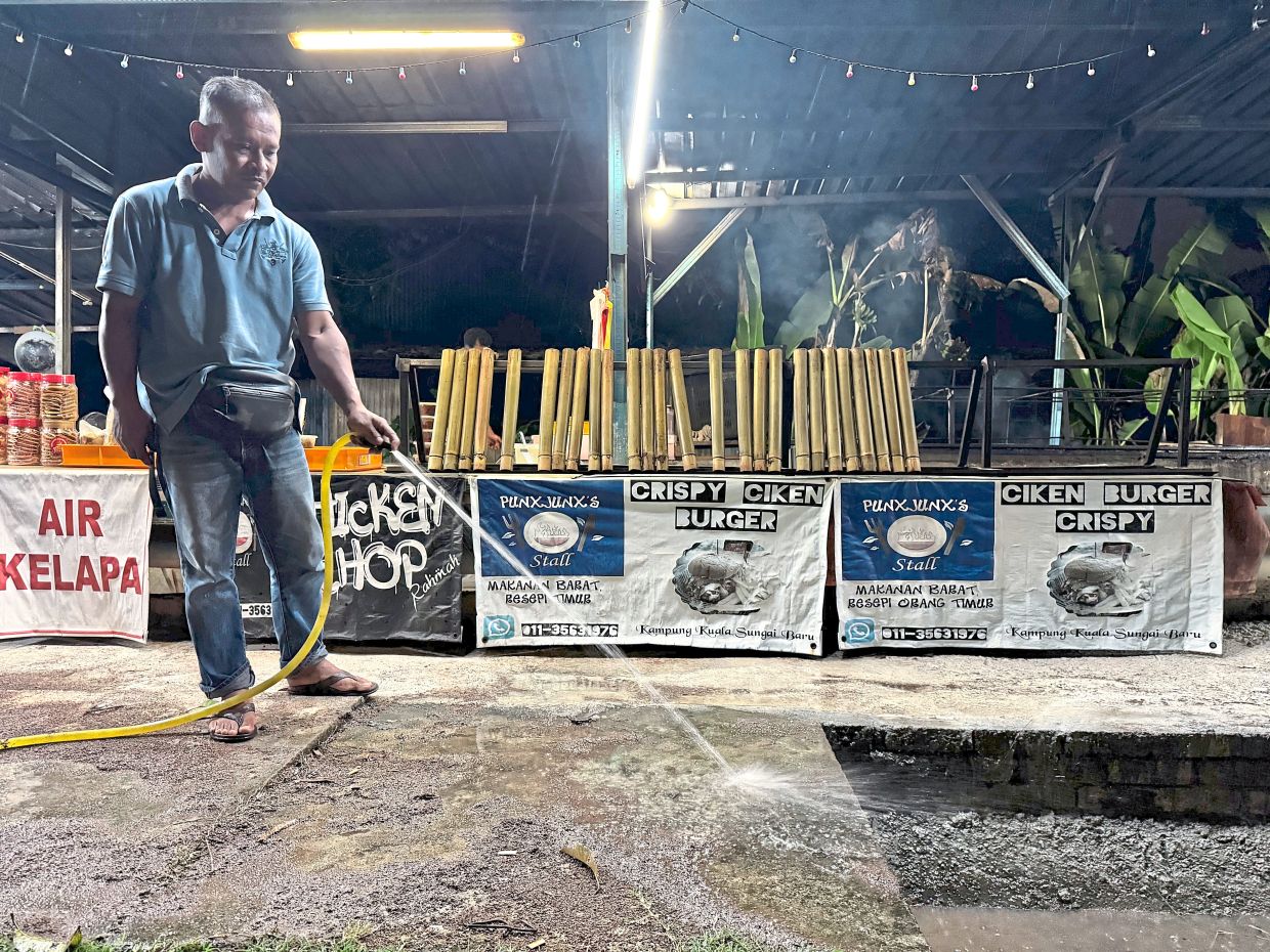 Azizi cleaning away dust on the road in front of his ‘lemang’ stall situated along the main road of the village.