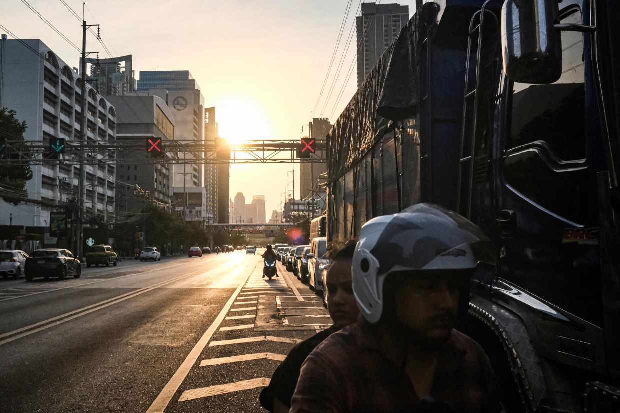 People ride their motorbike past vehicles waiting in traffic line at sunset in Bangkok. --Photo by Amaury PAUL / AFP