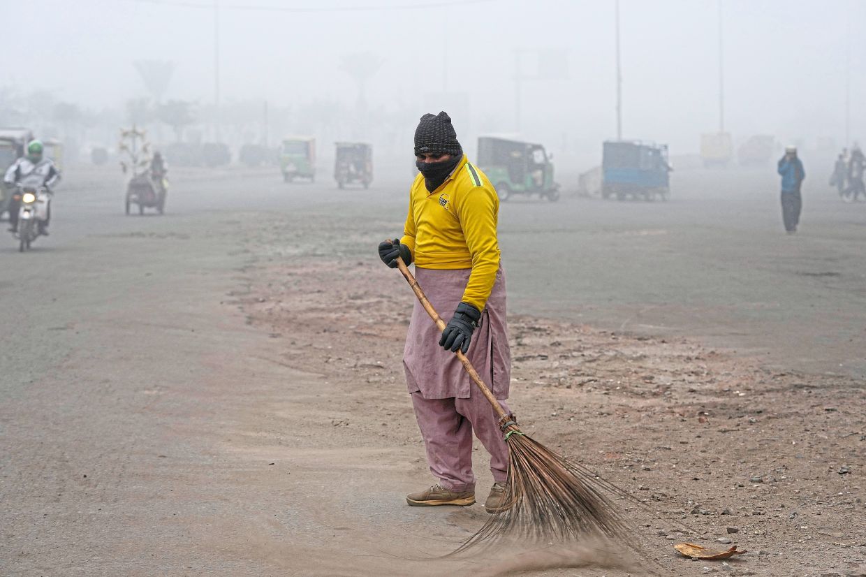 Braving the smog: A sweeper cleaning the streets as smog envelops the area and reduces visibility in Lahore. — AP