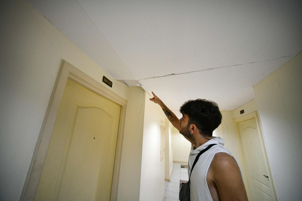 Turkish national Yigit Buyukergun pointing to a crack in the ceiling of his high-rise condo building. - AFP