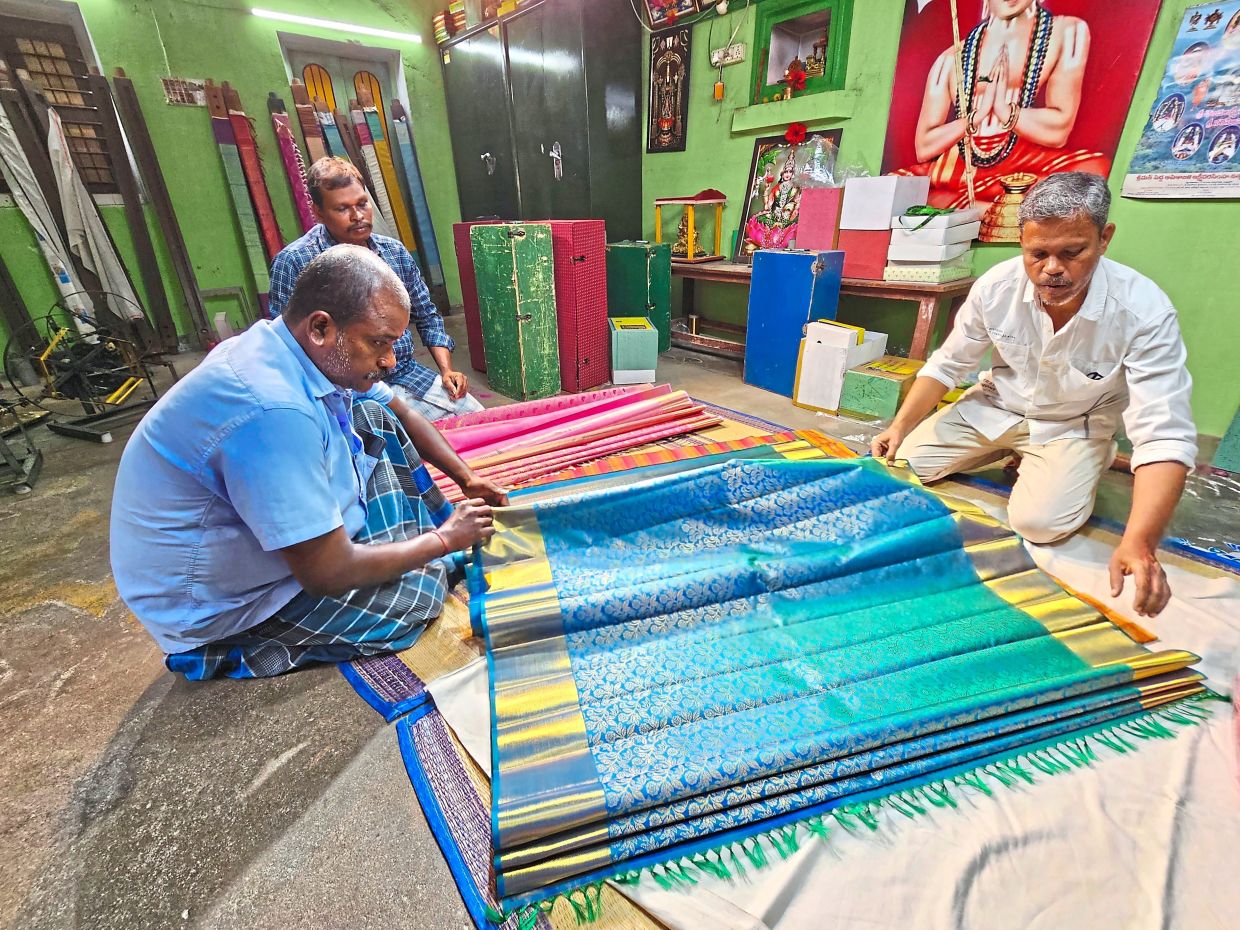 S. Kannadhasan, 53, (right) showing the various gold threaded silk sarees made by the weavers in Kanchipuram.