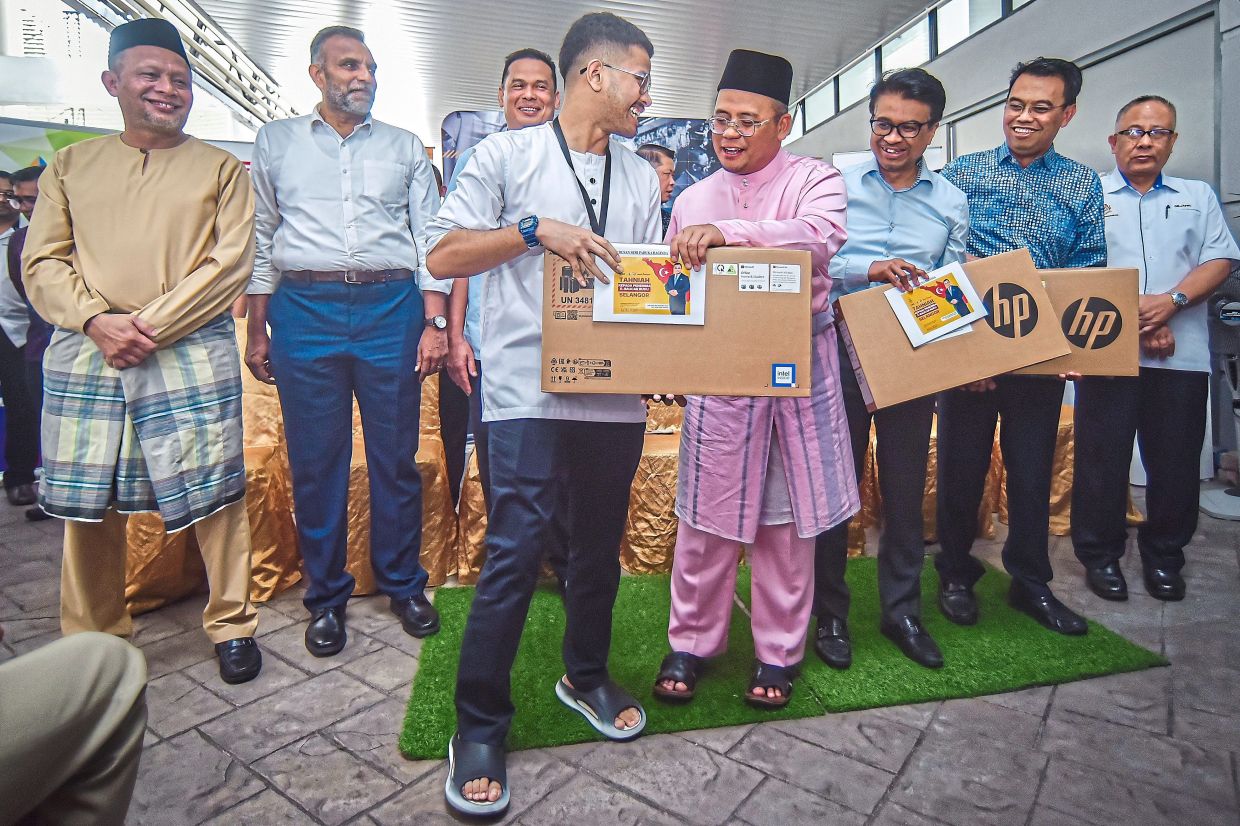 Rebuilding lives: Amirudin (fourth from right) handing over cash aid and laptops to 35 secondary school students at the Putra Heights mosque relief centre. — Bernama