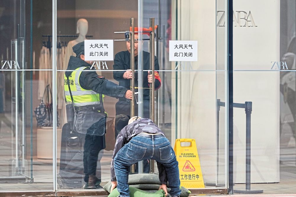 Security personnel securing a glass doorwith locks and sandbags near signs which reads ‘WindyWeather, This Door Shut’ in Beijing.- AP