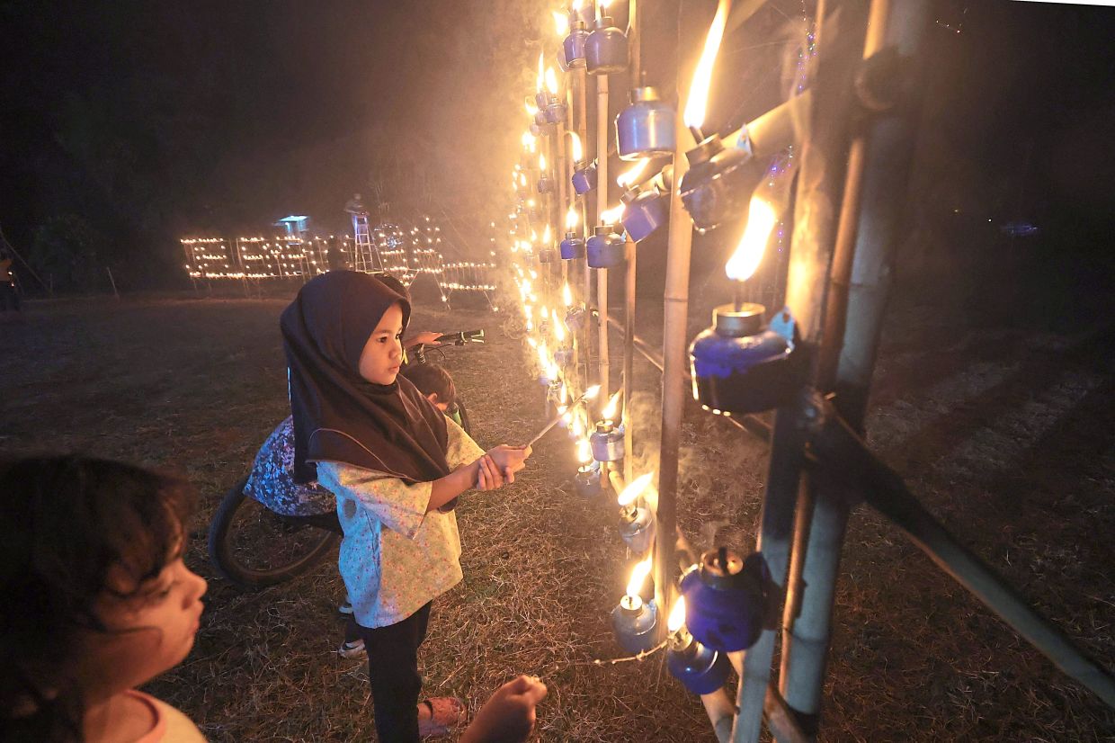 Youngsters enchanted by the oil lamps put up in the village in Perlis. 
